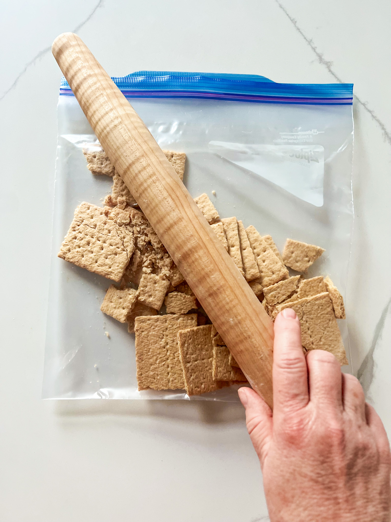 Hand using a rolling pin to pound graham crackers in a plastic bag