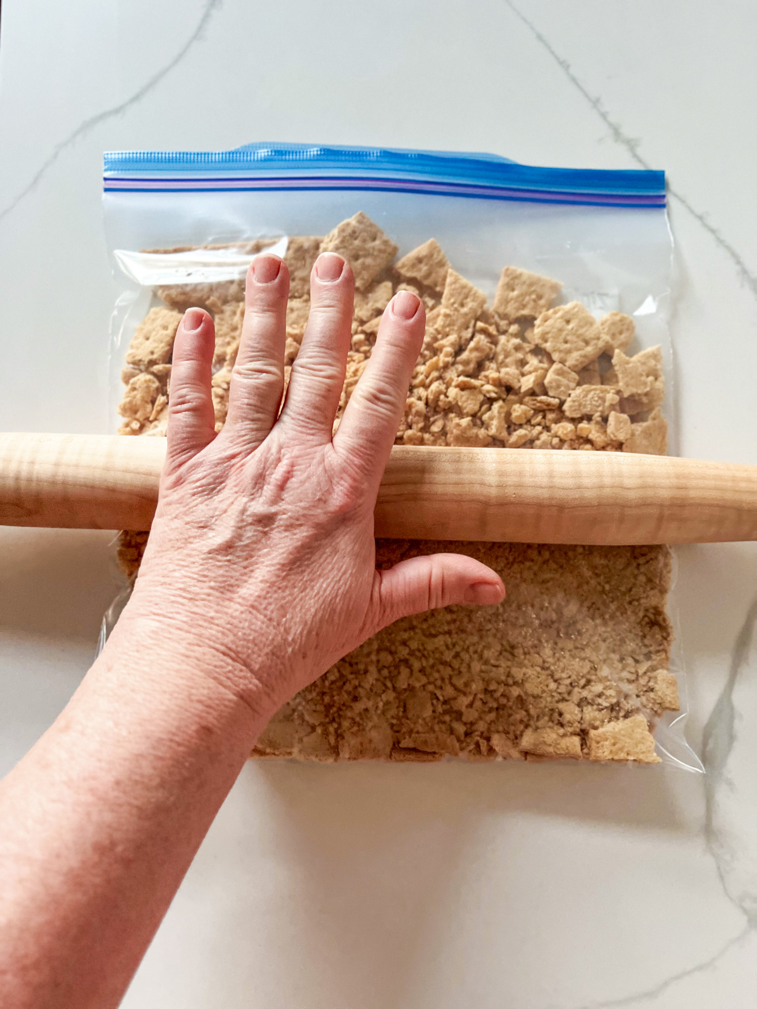 Hand using a rolling pin to crush graham crackers in a plastic bag