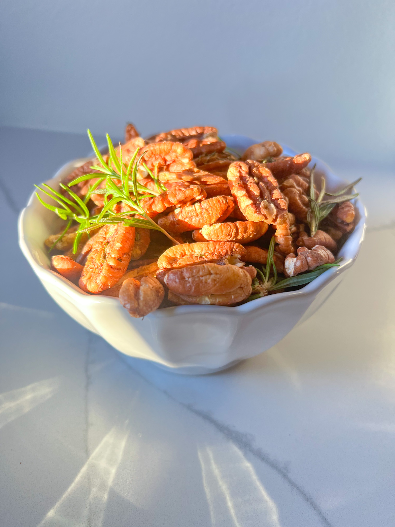 a white bowl with roasted pecans and rosemary