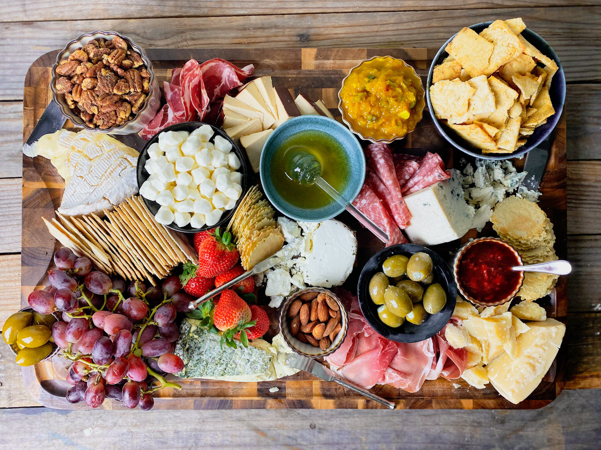 Large Charcuterie board with grapes, strawberries, meats and cheeses, olives, crackers honey, nuts and chutney.