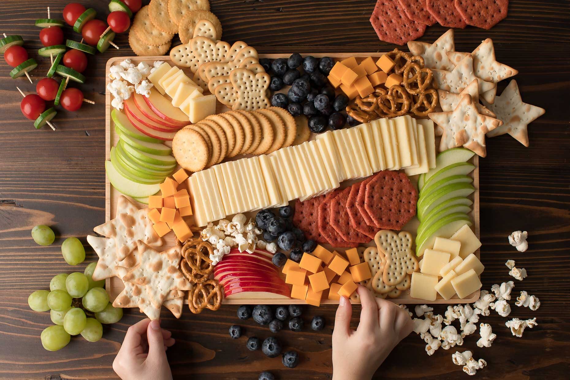 kid friendly cheese board recipe with crackers, fruit, popcorn and cheese and little hands