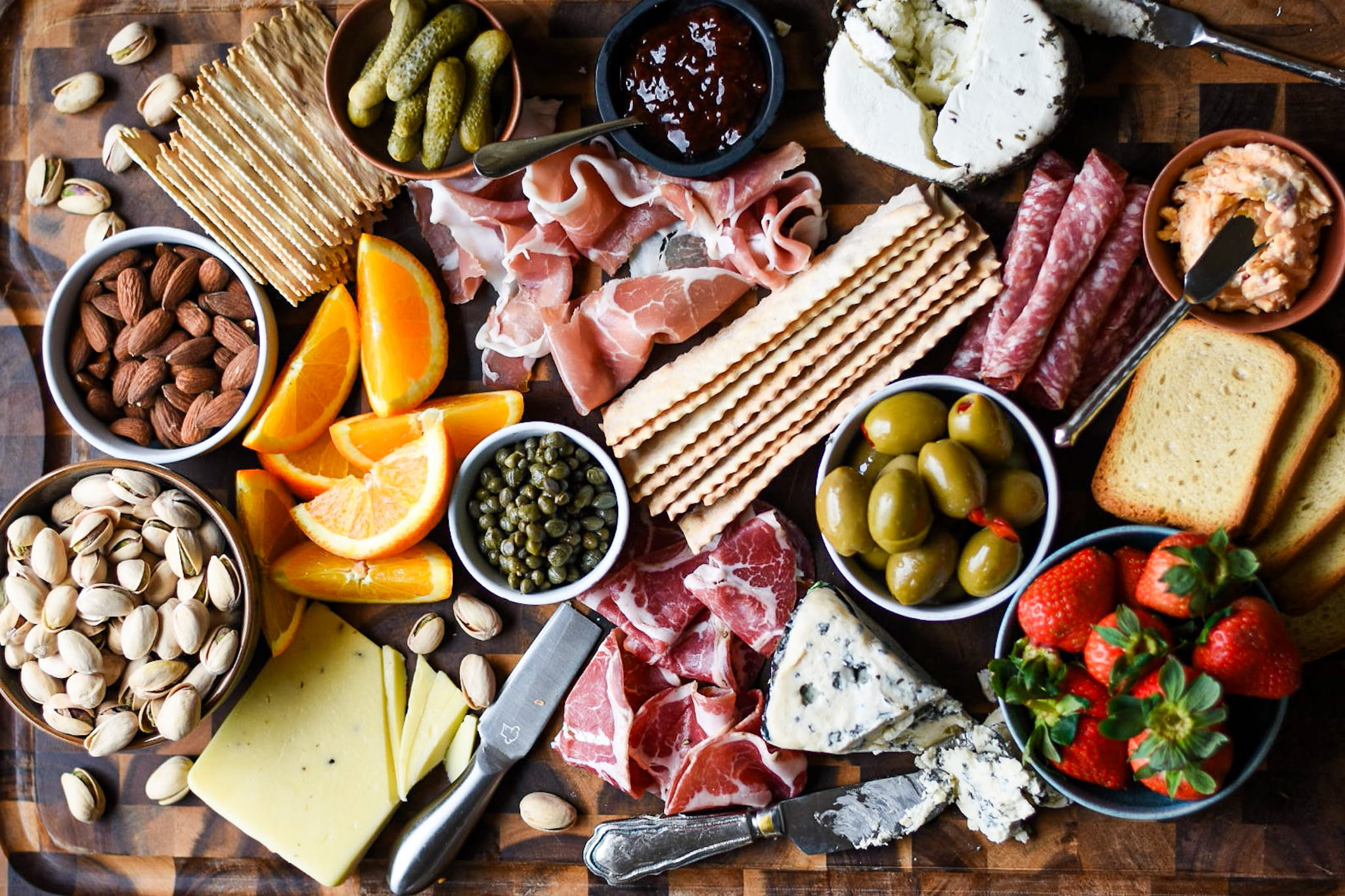 Charcuterie board with oranges, strawberries, crackers, pickles, nuts, meats and cheeses