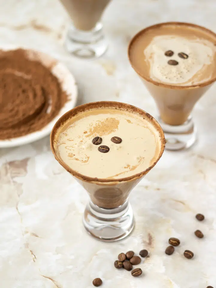 2 Espresso Martini Mocktails with coffee beans floating on top and a plate of espresso powder