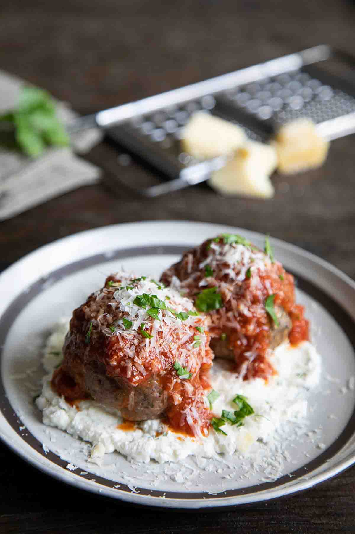 2 large meatballs on ricotta on a plate with tomato sauce