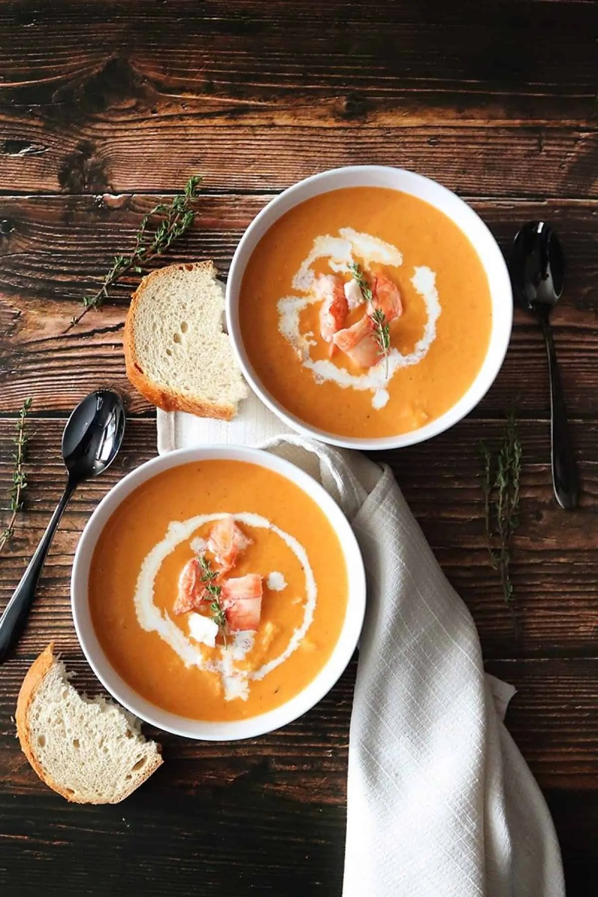 Two bowls of lobster bisque with bread and a white napkin and spoons
