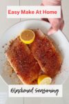 Blackened seasoning on white fish with 2 lemon halves on a plate, and a hand holding it