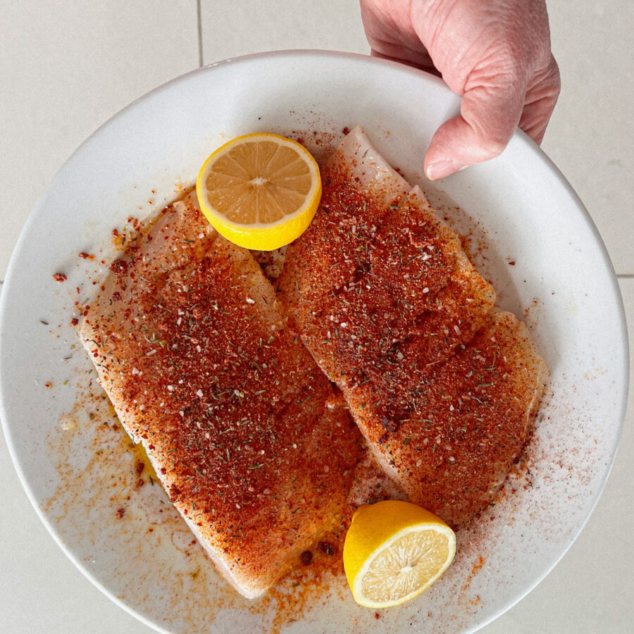 blackened seasoning on white fish with 2 lemons on a plate, a hand holding it
