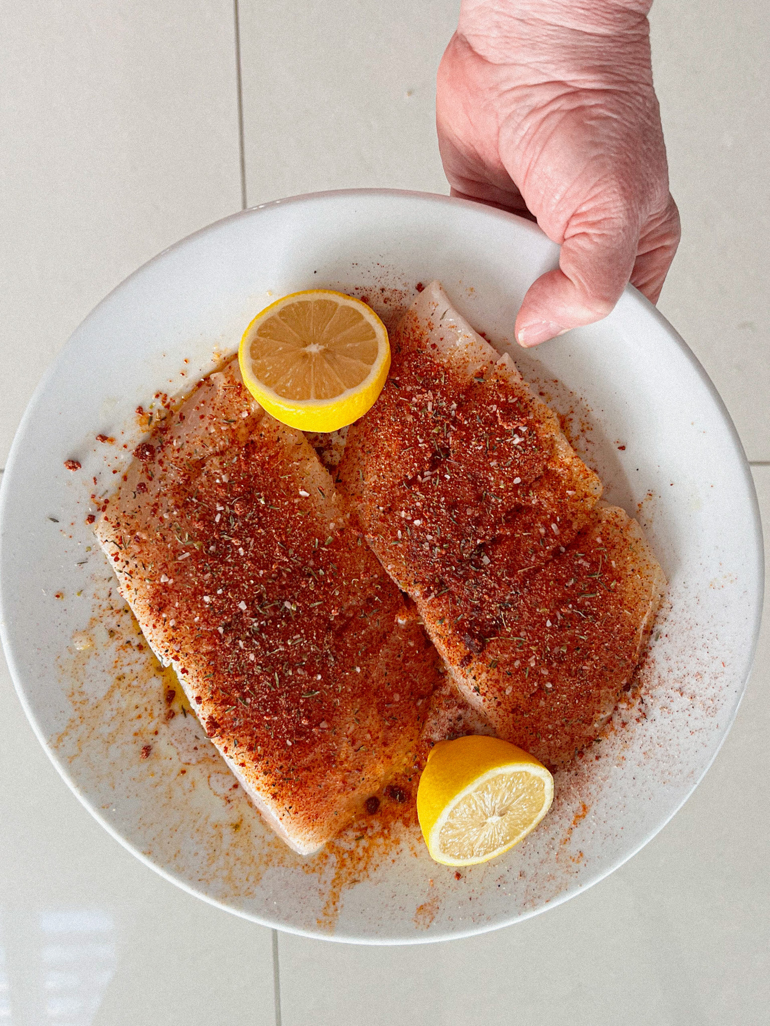 blackened seasoning on white fish with 2 lemons on a plate, a hand holding it