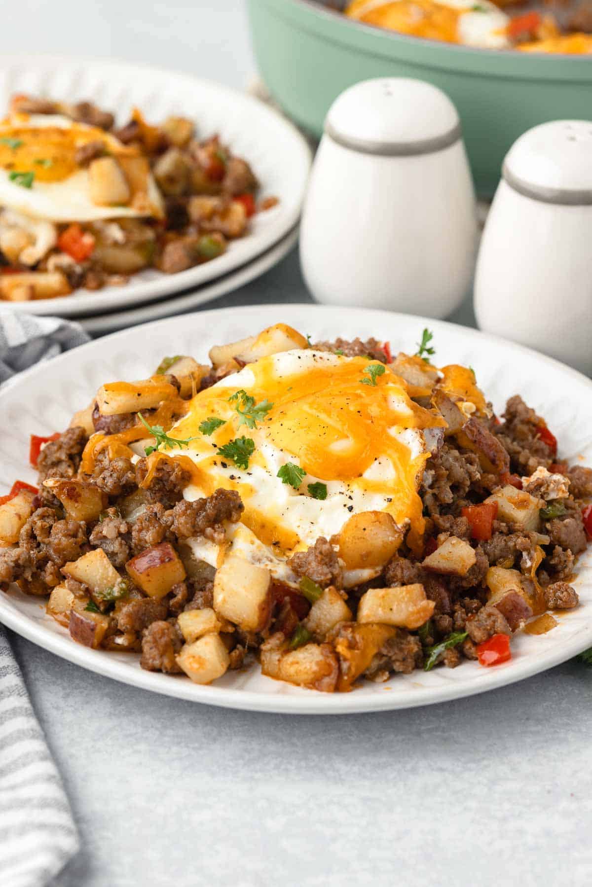 Breakfast sausage potato hash on a plate with a runny egg on two plates with salt and pepper