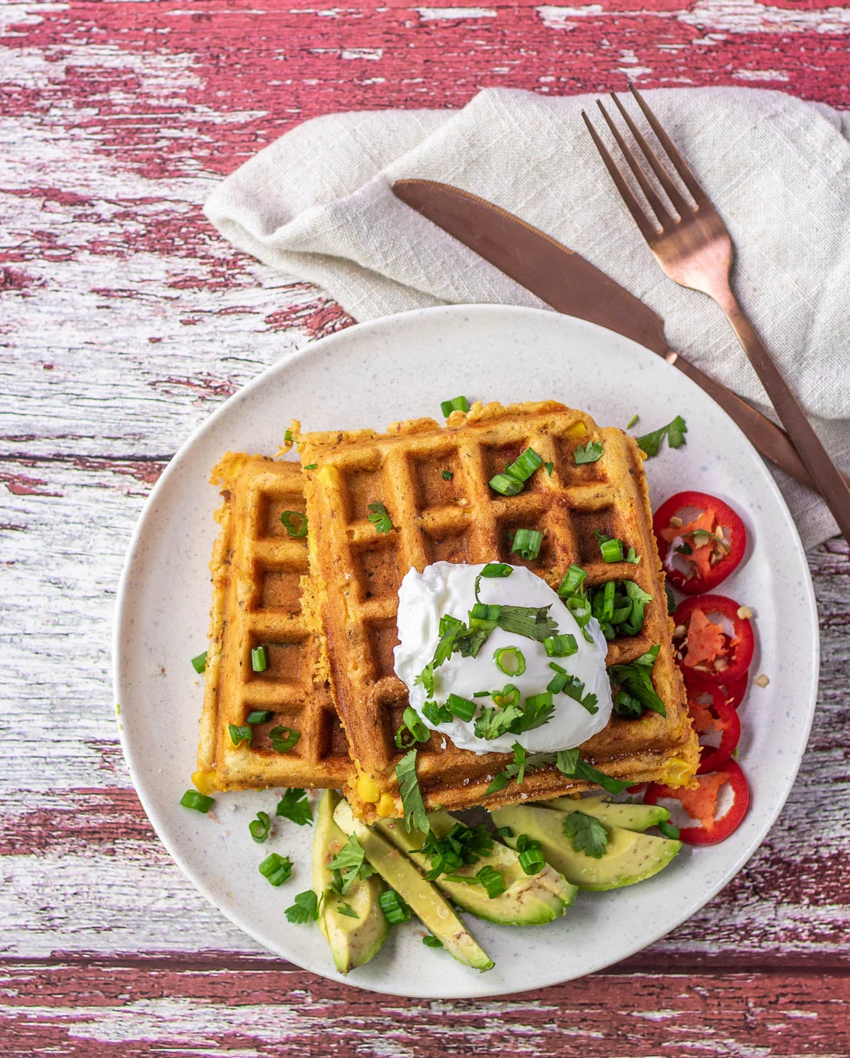 Mexican waffles with chorizo and avocado and tomato on a plate with a knife and fork and napkin