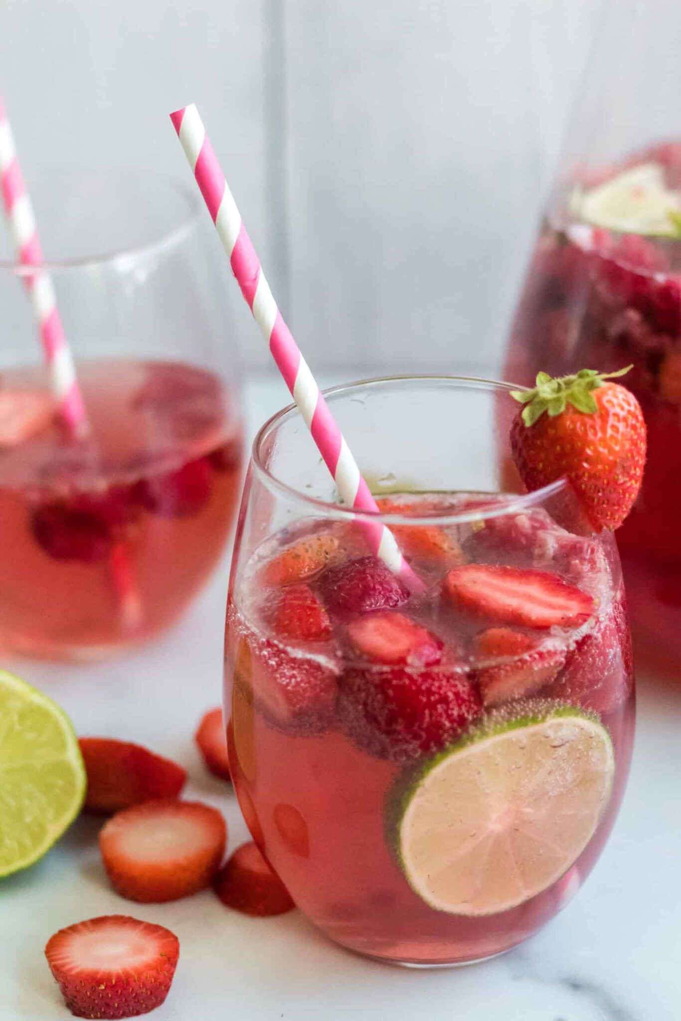 Pink Moscato Sangria in 2 glasses with red and white straws and a pitcher of sangria