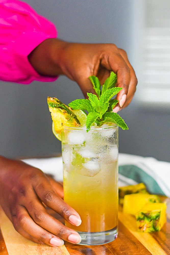 Hand reaching for mint on a pineapple brown sugar mojito with a straw
