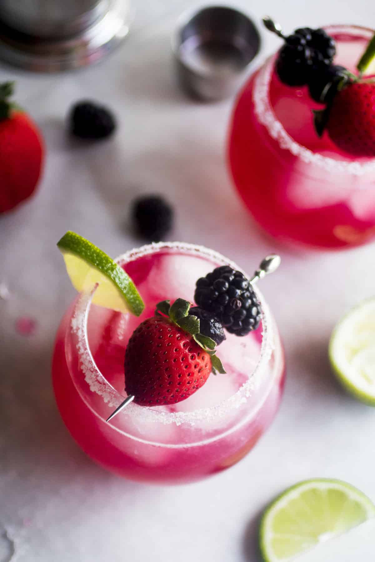 triple berry margaritas in two glasses with limes and berries