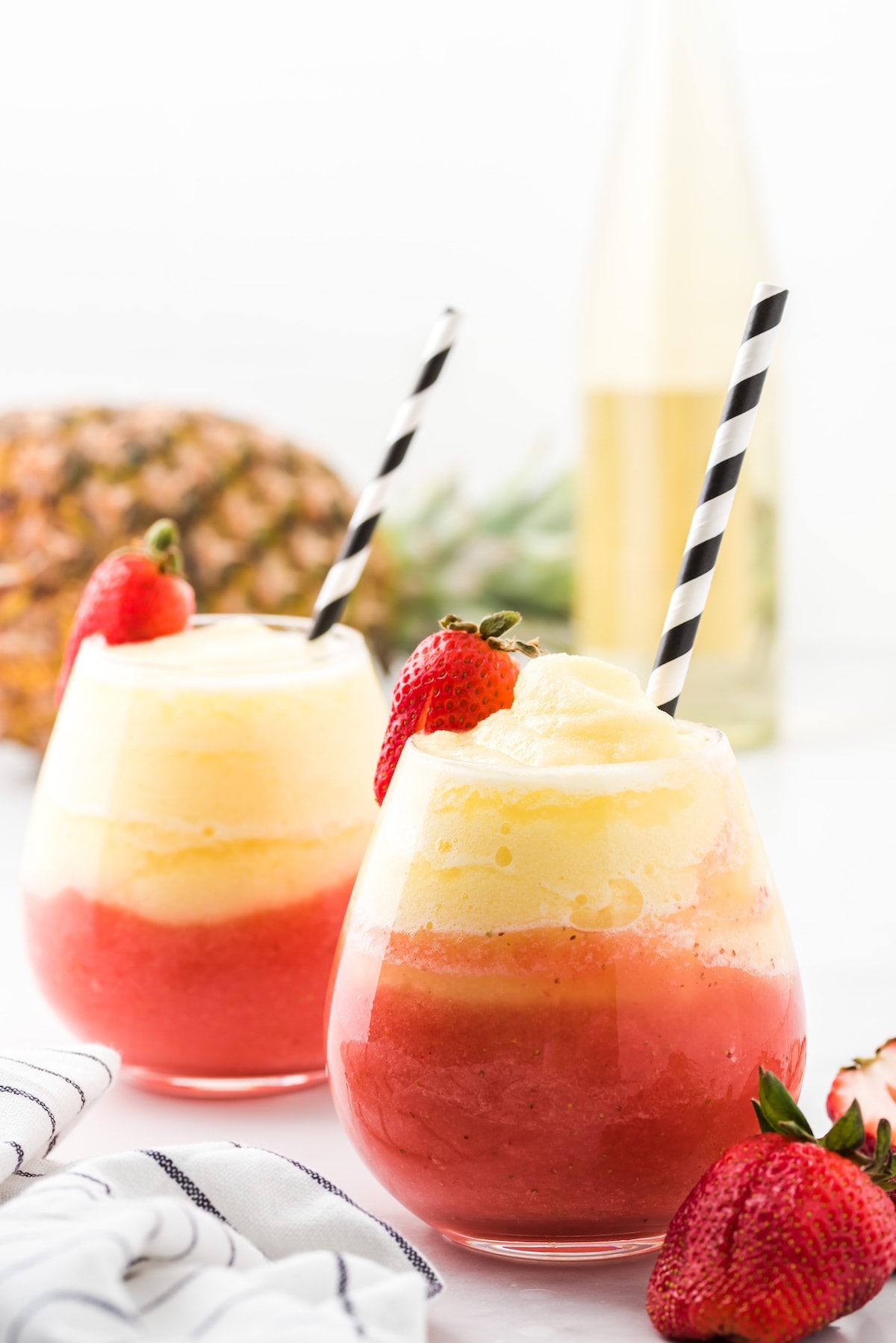 white wine slushies in 2 glasses with strawberry and straws