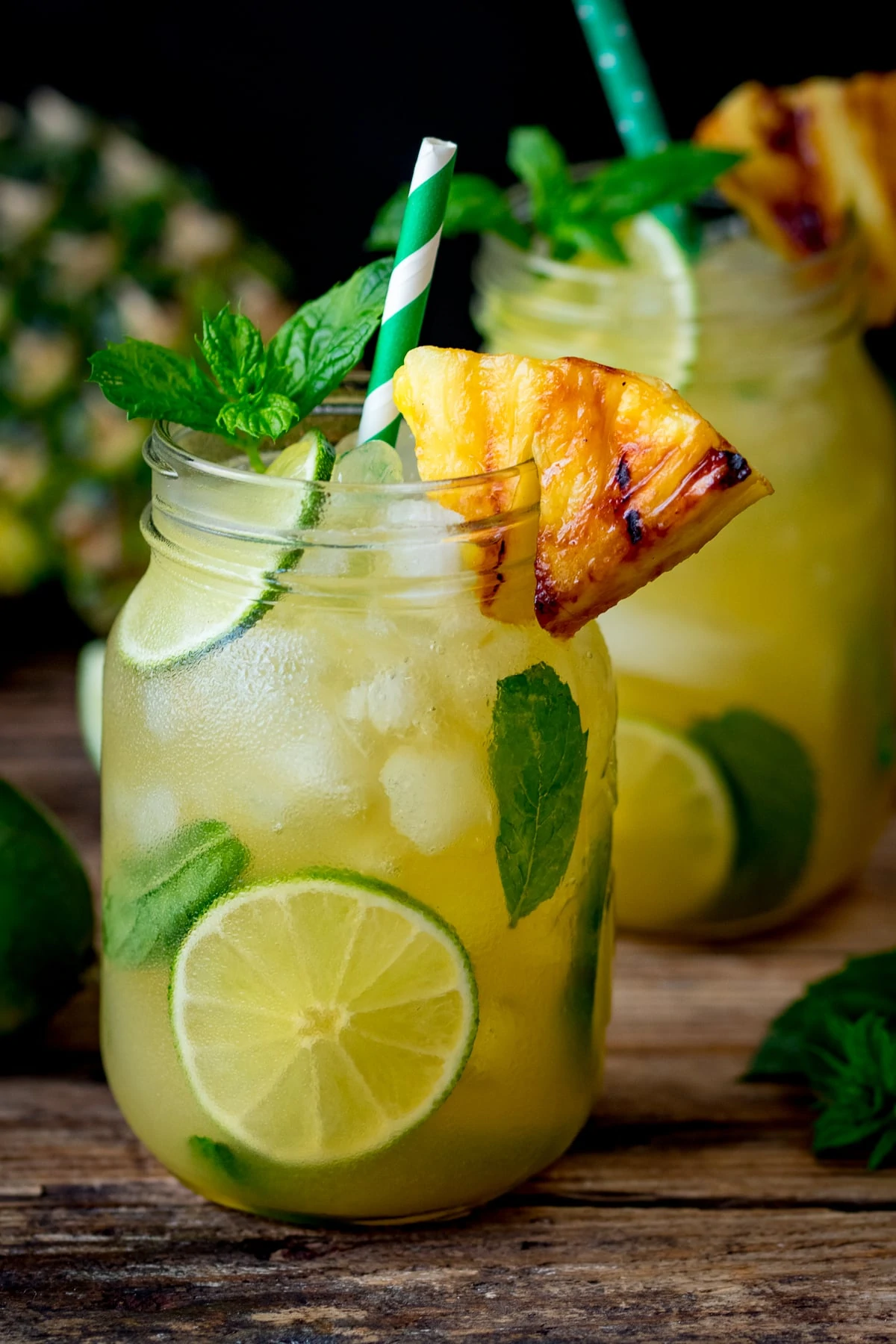pineapple and ginger mojitos in jars with straws and pineapples and limes